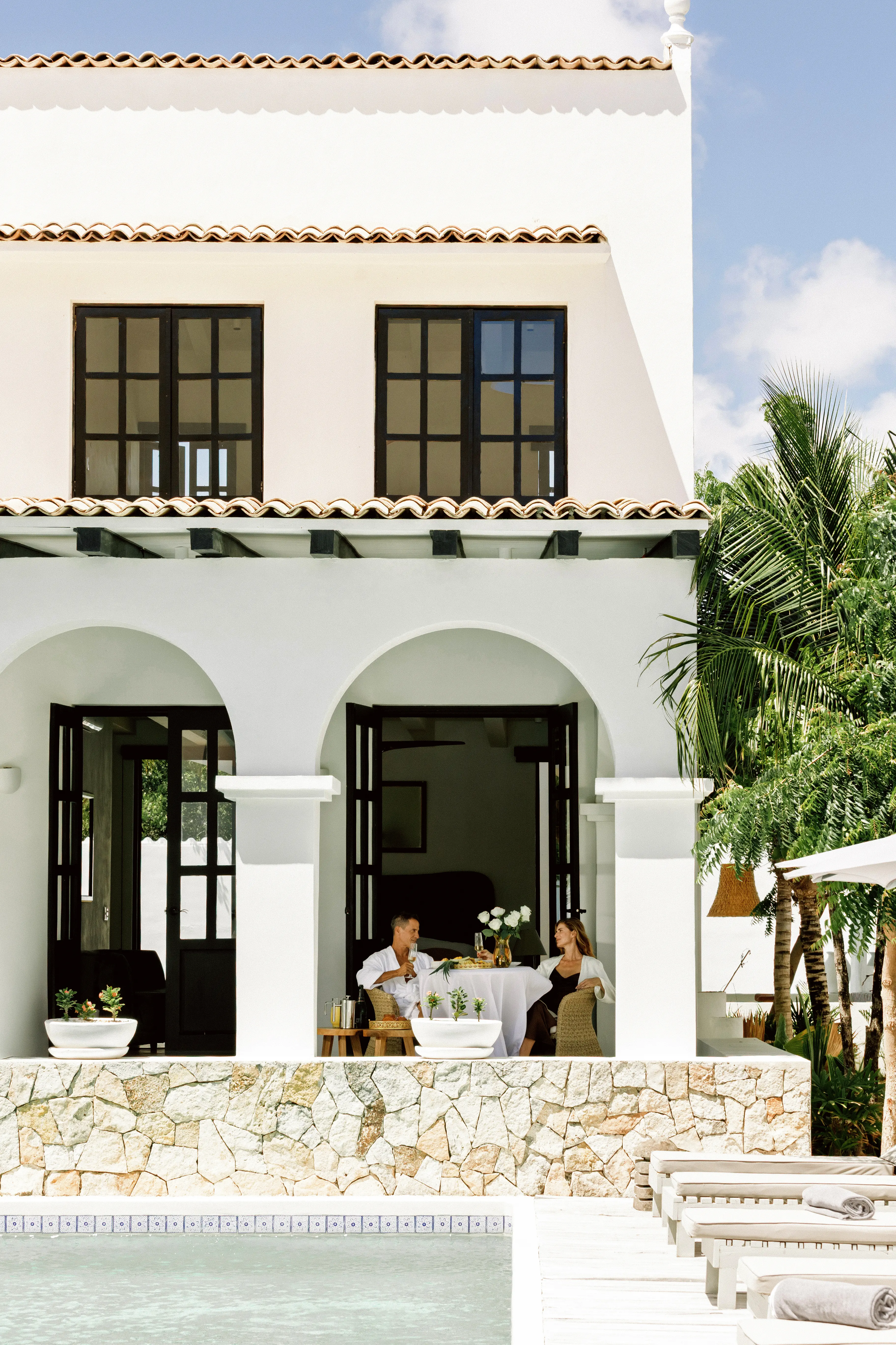 Couple dining poolside at an L'TOPIA villa with arches and tropical gardens